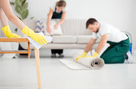 due addetti alle pulizie un uomo e una donna puliscono il salone di un'appartamento con divisa bianca e verde guanti gialli la donna pulisce il dvano l'uomo il tappeto